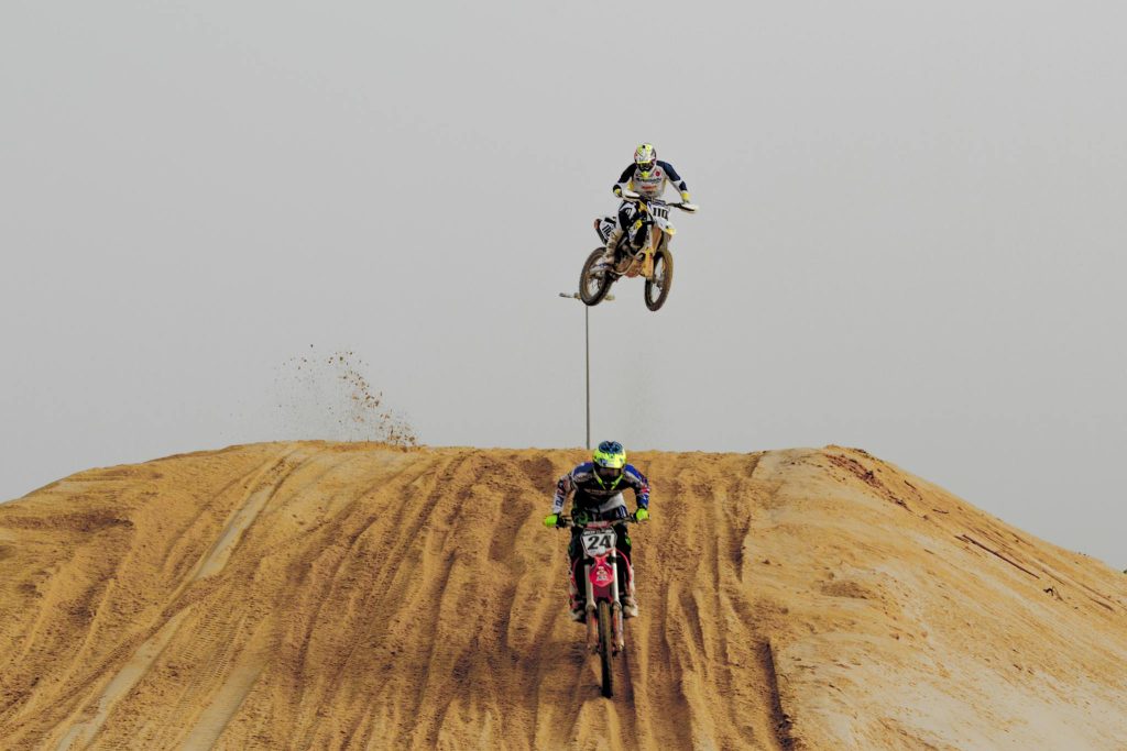 Thrilling motocross competition on a sandy track with bikers in action against a clear sky.